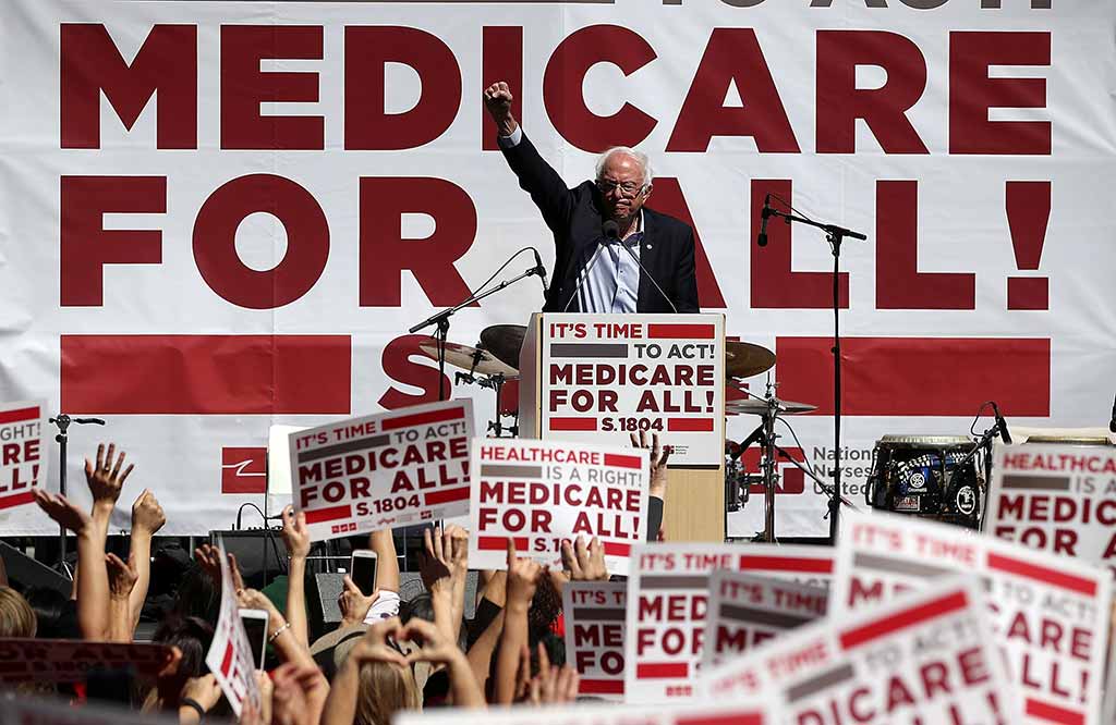 Bernie Sanders in front of a Medicare For All Banner
