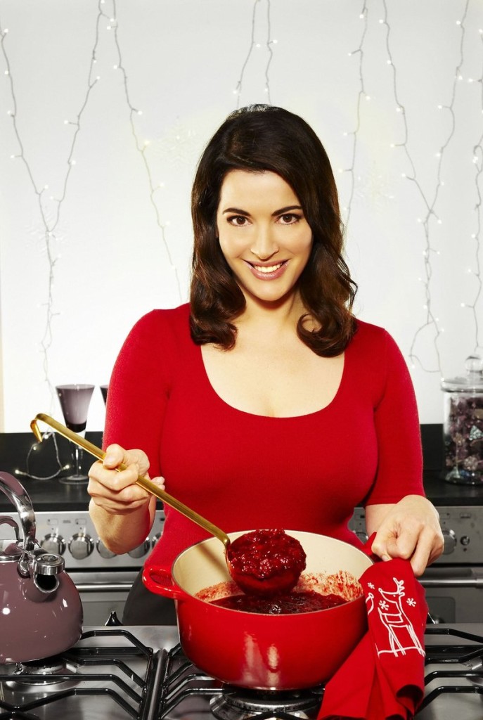 Nigella Lawson stirring something red and saucy in a dutch oven and smiling at the camera.