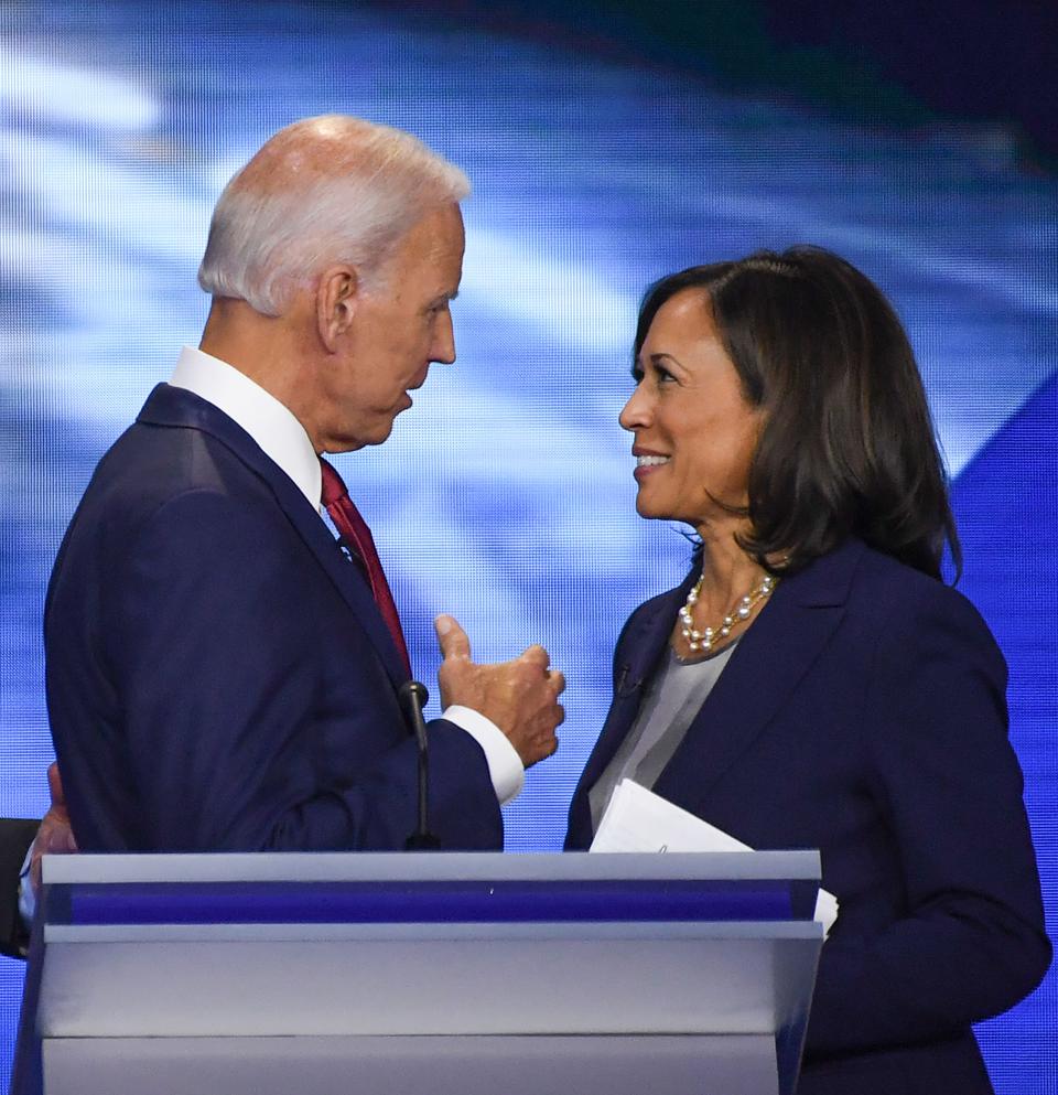 Joe Biden and Kamala Harris talking to each other behind a podium
