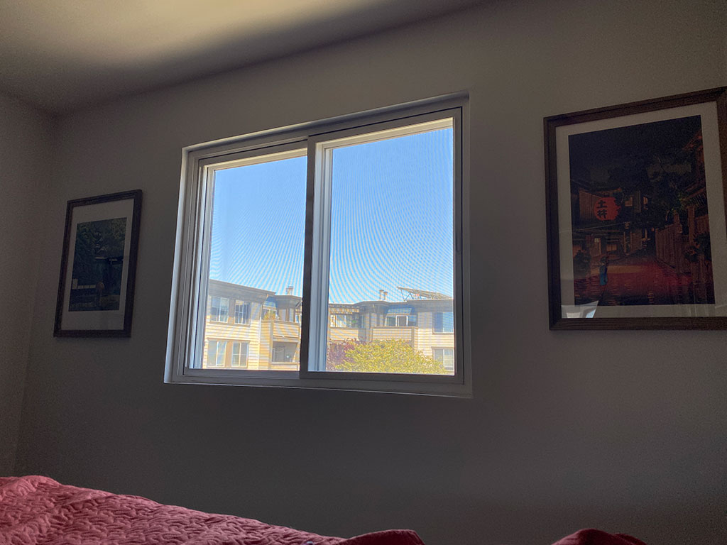 View from my bed through my window to see another residential complex across the street and a clear blue sky.