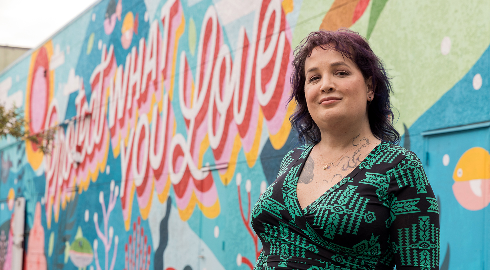 Corry Frydlewicz stands in front of Emeryville's Protect What You Love mural