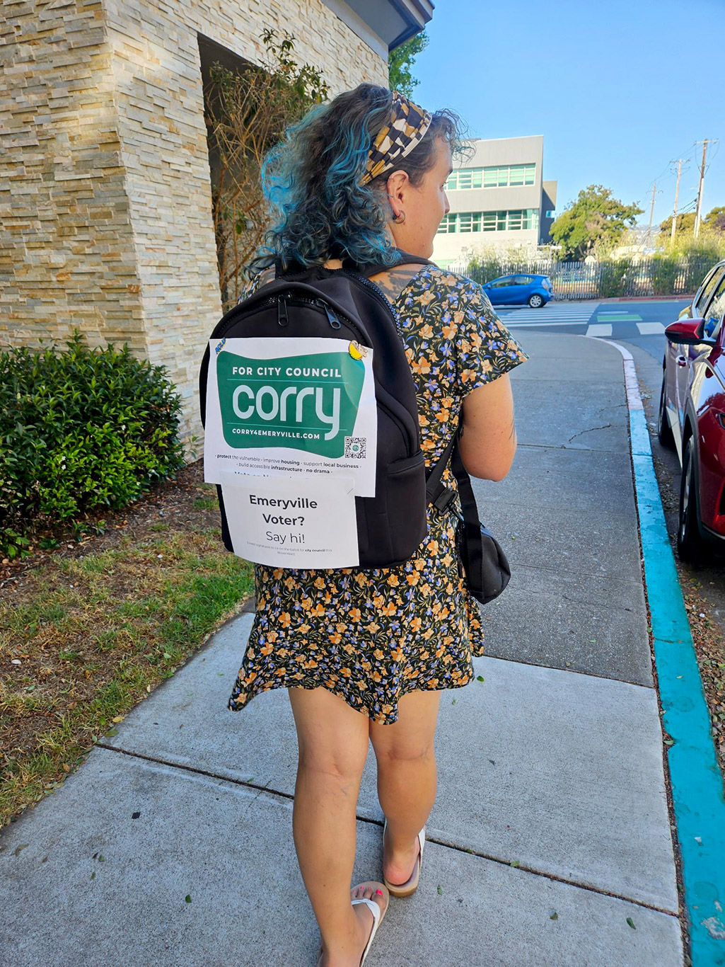 Corry Frydlewicz gathers signatures to be on the ballot for Emeryville City Council, wearing a backpack with a home-printed sign pinned to it.