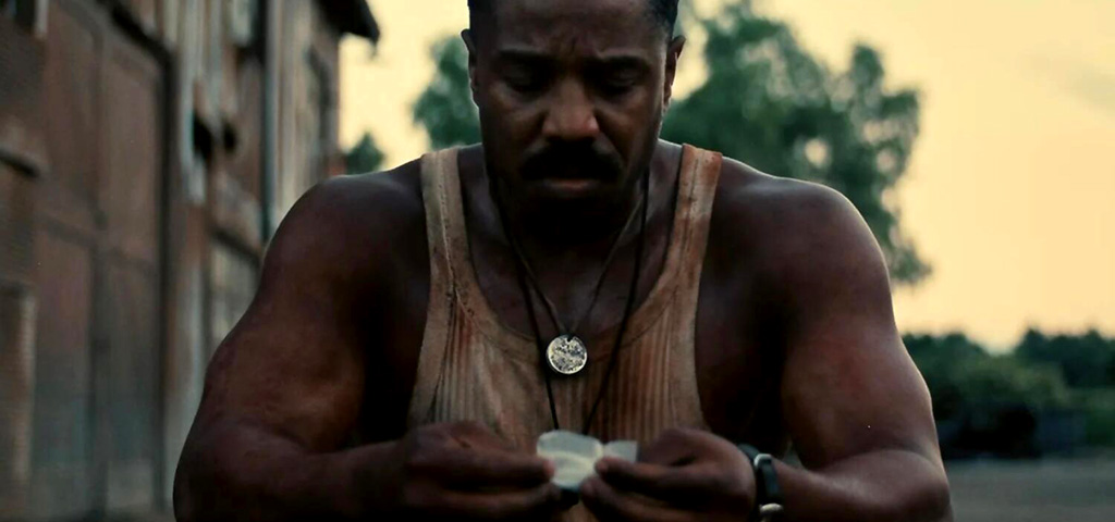 Michael B. Jordan shakily assembled a cigarette while wearing a bloodied tank top outside the building in Sinners.